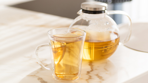 Teezubehör Glaskanne und Glastasse mit hellgoldenem Tee auf einer hellen Tischplatte