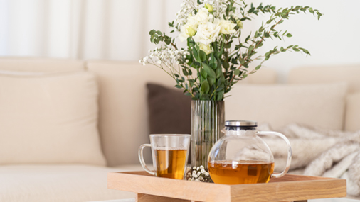 Frühlingstees Glaskanne und Glas mit goldfarbenem Tee auf einem Holztablett mit Blumenvase