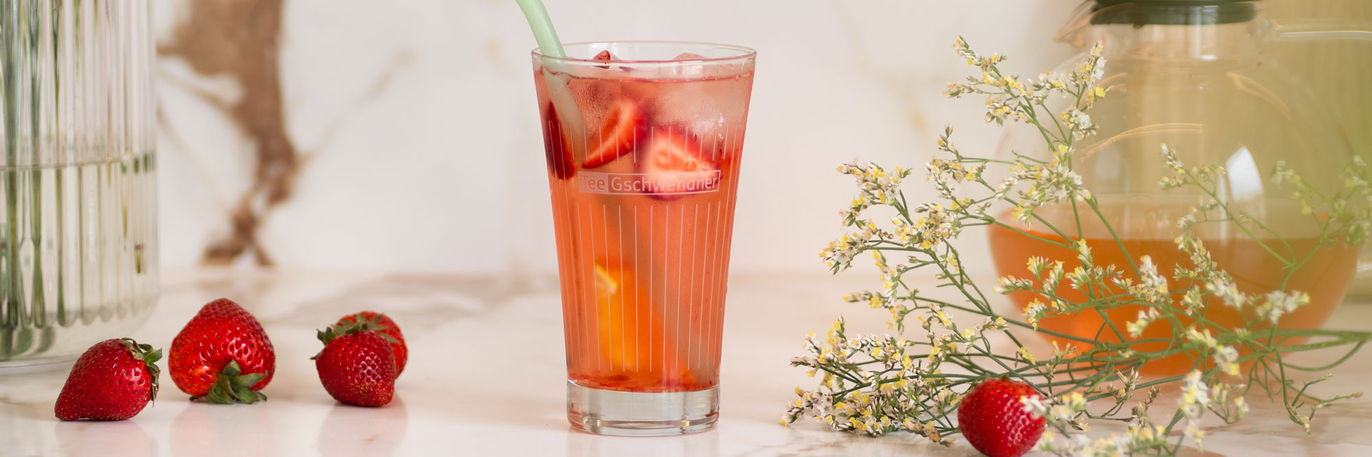 Glas mit Erdbeer-Eistee, Erdbeeren und Blüten auf Tisch