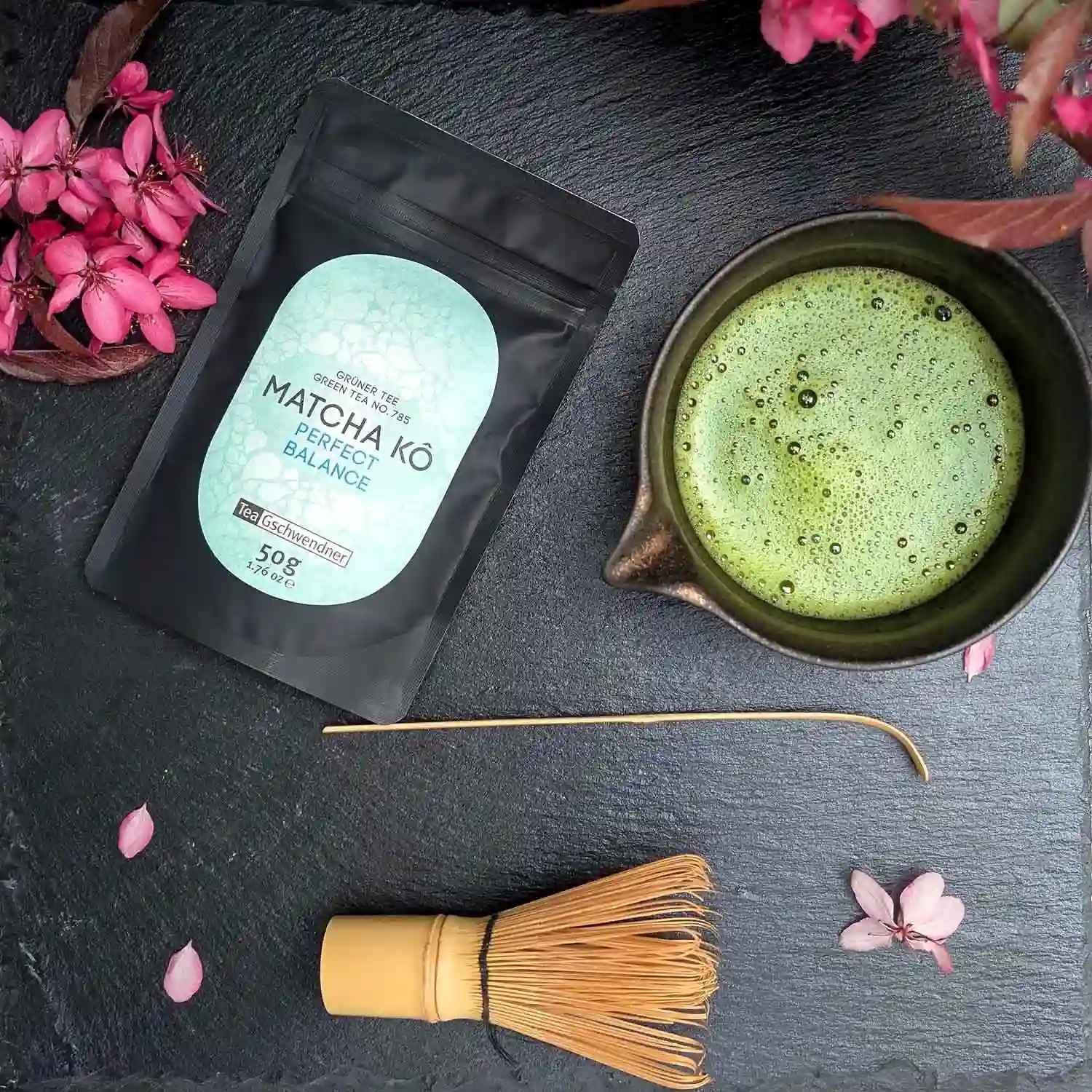 Japan Matcha Kô "Perfect Balance" im 50-g-Beutel neben aufgeschäumter Matcha-Schale und Bambusbesen – ausgewogener japanischer Matcha für puren Genuss, Latte und Desserts