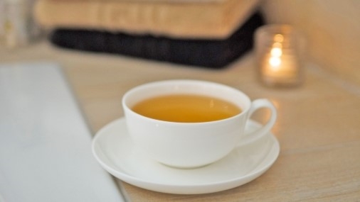 Teetasse mit hellem Schwarztee auf Holztischplatte mit gefalteten Frotteetüchern und Teelicht im Hintergrund