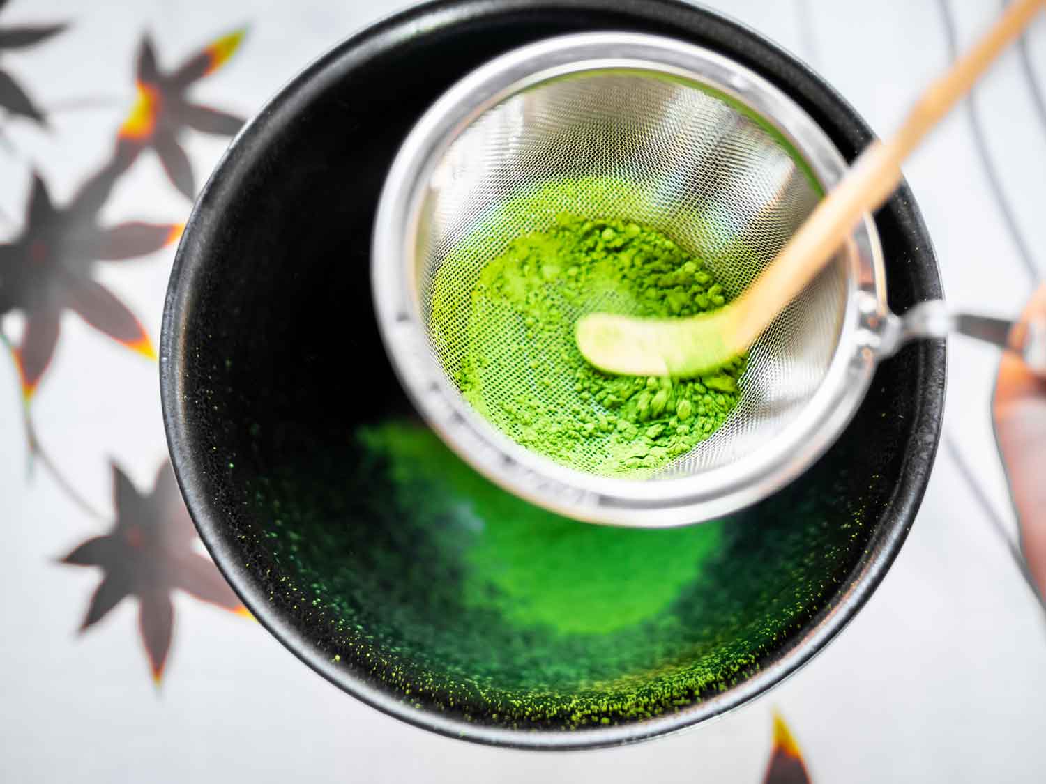 Grünes Matcha Tee Pulver wird durchs Sieb in schwarze Schale