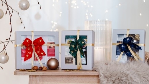 Teegeschenke Drei weihnachtlich gestaltete Tee-Präsente in hellgrauen Kartonschachteln auf einem hellen Holztisch