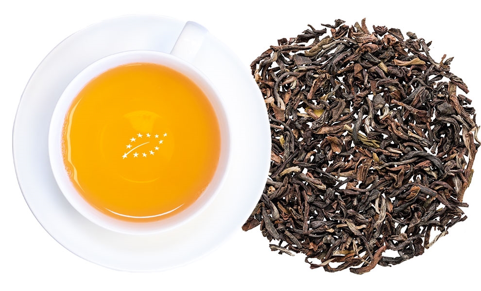 Weiße Tasse Schwarztee neben losen Teeblättern