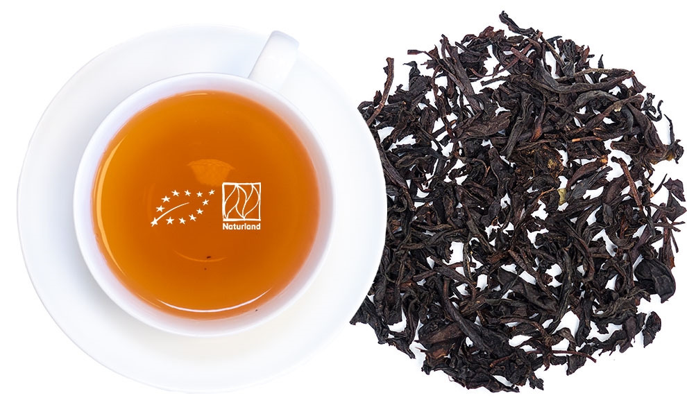 Weiße Tasse mit schwarzem Tee und losen Teeblättern