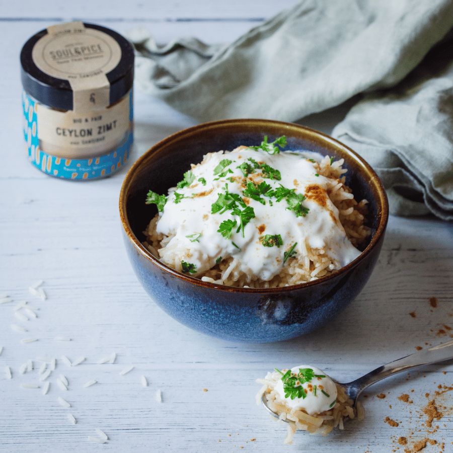 Keramikschale mit würzigem Reis, cremigem Joghurt, frischen Kräutern und SoulSpice Ceylon Zimt auf hellen Holztisch