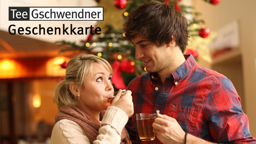 Junge Frau und junger Mann mit Teetassen in den Händen blicken sich an vor weihnachtlichem Hintergrund