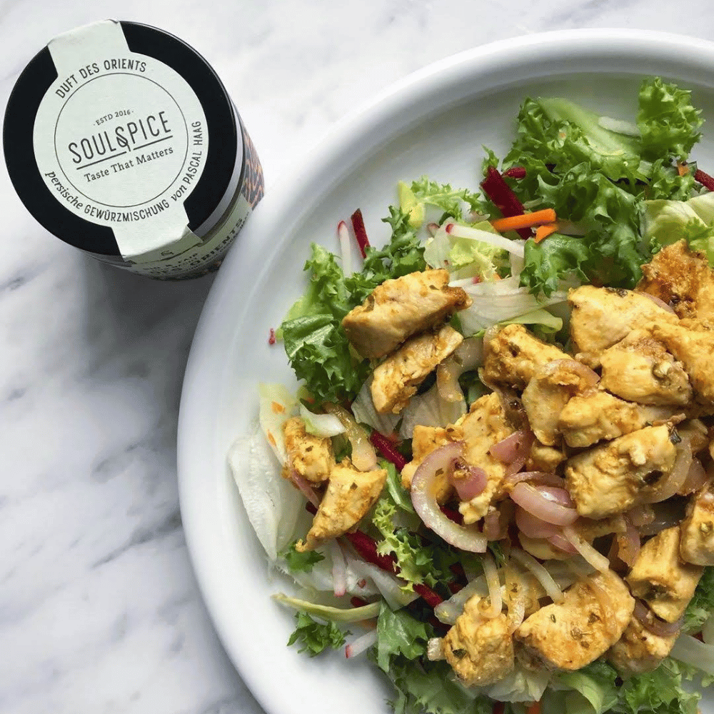 Teller mit gemischtem Blattsalat, Gemüse und mariniertem Hähnchenfleisch, daneben eine Dose SoulSpice persische Gewürzmischung