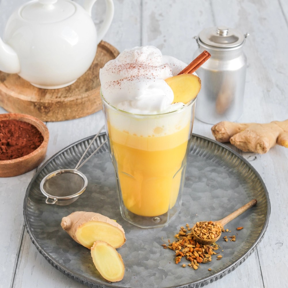 Glas Kurkuma-Ingwer-Latte mit Milchschaum und Zimt