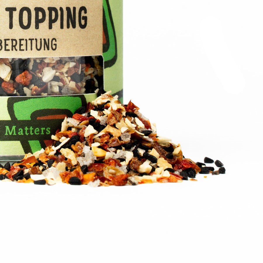 Offenes Glas mit bunter Gewürztopping-Mischung, die sich dekorativ auf der weißen Fläche verteilt