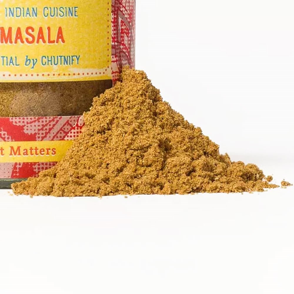 Häufchen Garam-Masala-Gewürzpulver vor einem bunten Gewürzglas