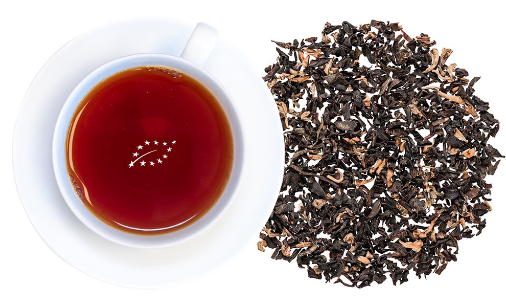 Weiße Tasse schwarzen Tees neben losen Teeblättern