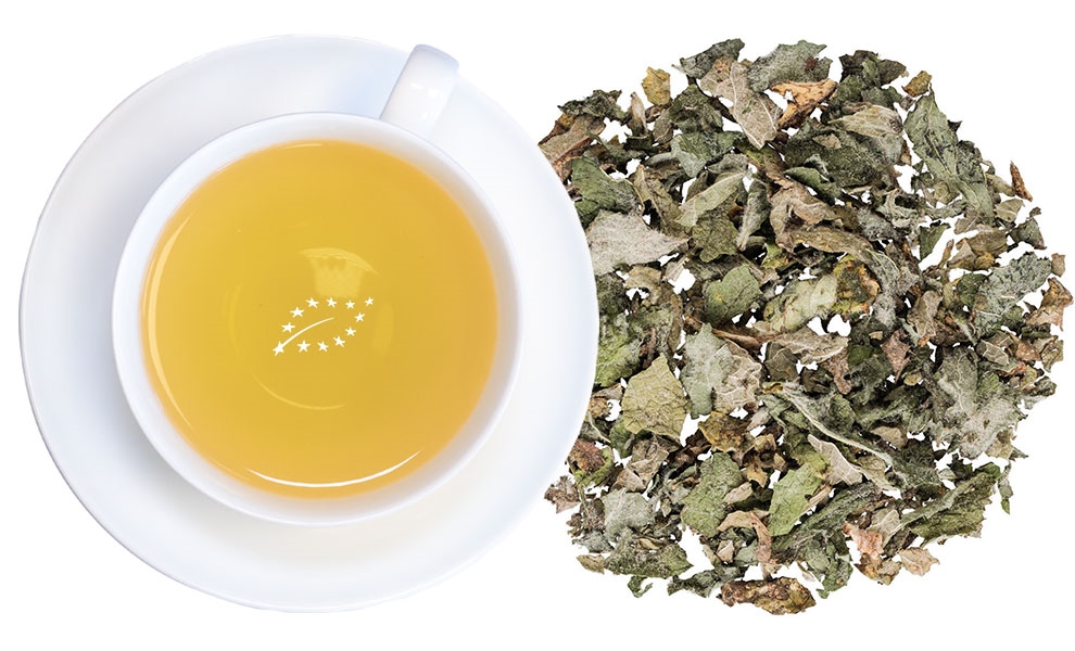 Weiße Tasse Kräutertee neben losen Teeblättern