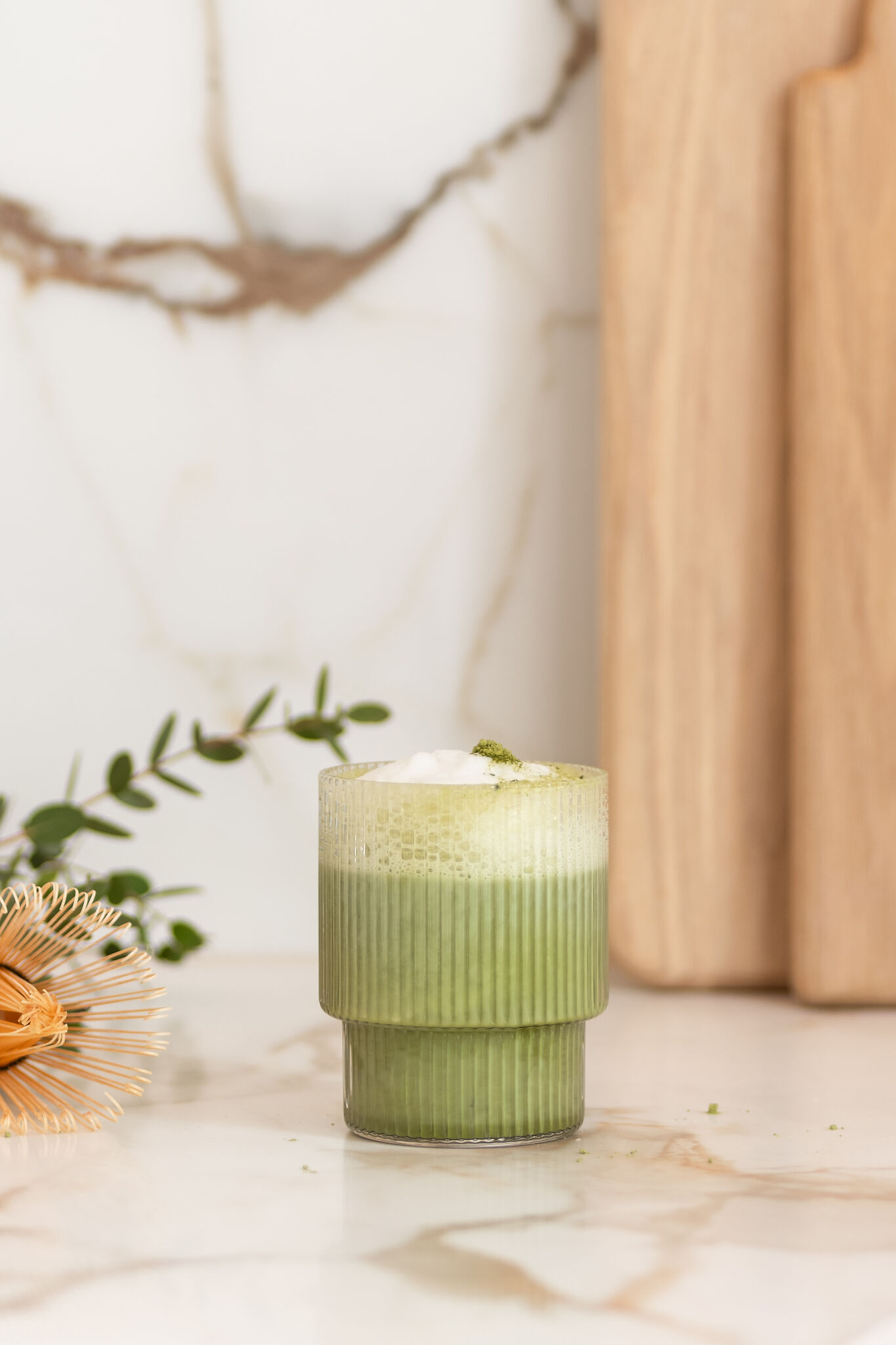 Grüner Iced Matcha Latte mit Milchschaum in einem geriffelten Glas, dekorativ auf einem Marmortisch arrangiert