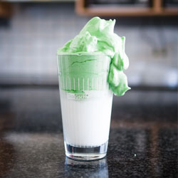 Hohe Glas mit weißer Milch und grünem Schaum im Kücheninteri