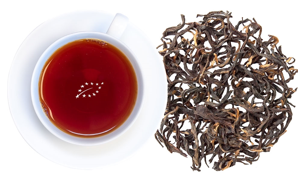 Weiße Tasse mit schwarzem Tee neben losen Teeblättern