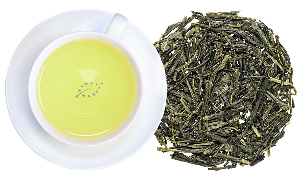 Tasse grüner Tee neben losen grünen Teeblättern