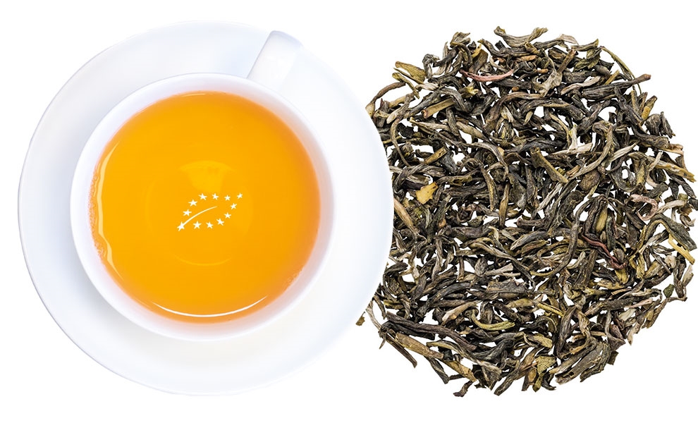 Weiße Tasse grüner Tee mit losen Blättern daneben
