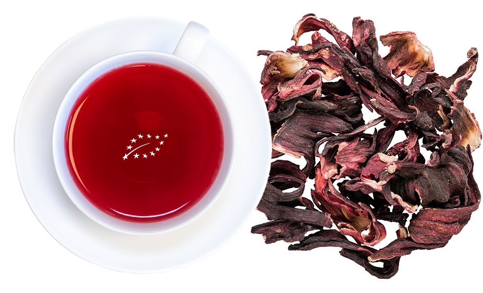 Rote Tasse Hibiskustee neben getrockneten Hibiskusblüten
