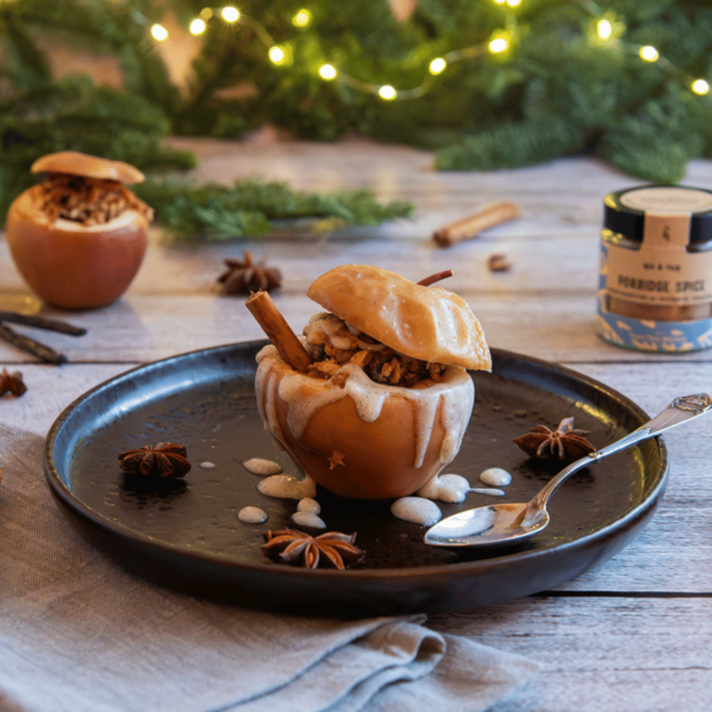 Nahaufnahme eines festlich angerichteten Bratapfels mit Nussfüllung, Zimtsauce und Sternanis auf schwarzem Teller vor weihnachtlicher Dekoration